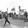 Black‑and‑white photograph of youths overturning and throwing deck chairs during a chaotic seafront disturbance, with crowds watching from the promenade.